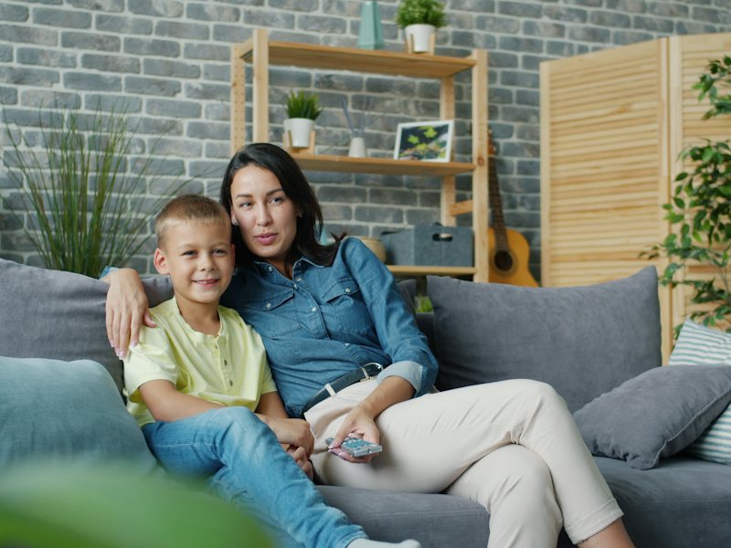 A parent and child watching something together on the sofa